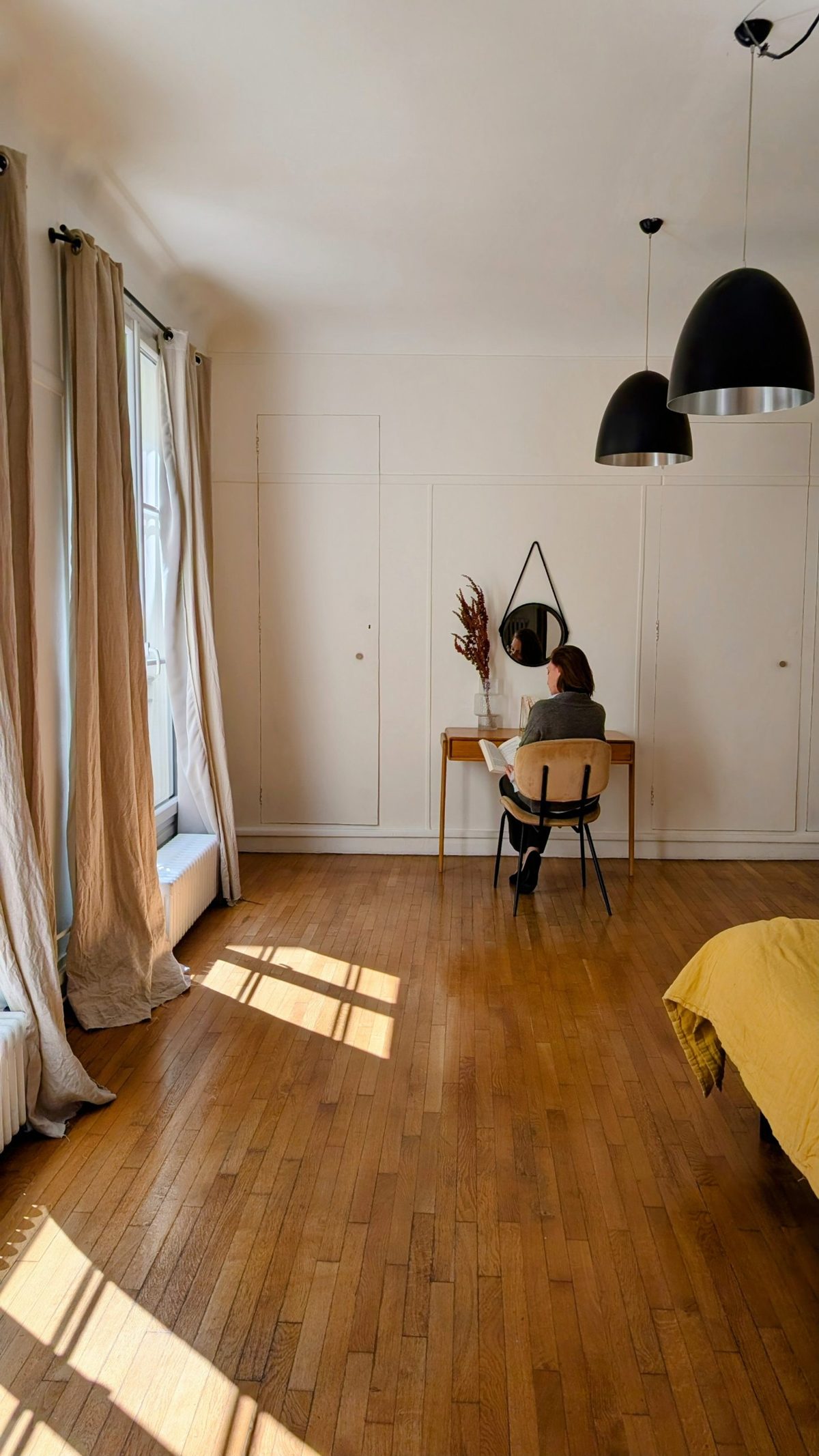 Appartement parisien baigné de soleil, parquet, rideaux en lin et une femme lisant à un bureau en bois