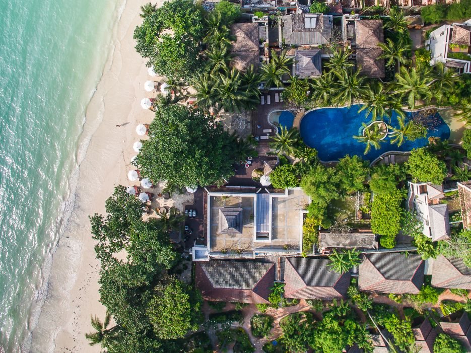Vue aérienne d’un resort en bord de plage à Koh Samui, avec piscine, jardins de palmiers et sable blanc